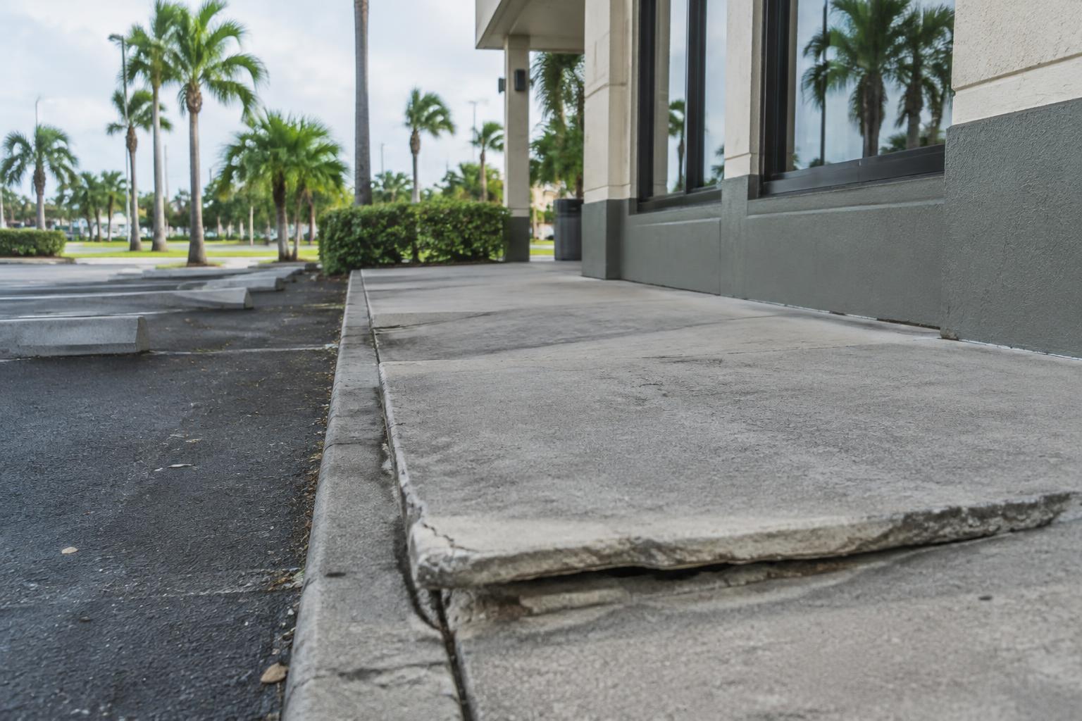 An uneven, cracked sidewalk creates a tripping hazard outside a Florida building.